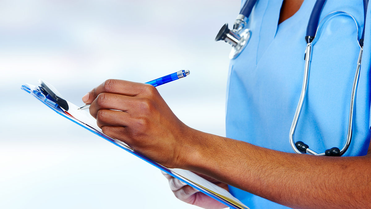 A Black nurse writing on a blue clipboard in blue scrubs. Only their arm, hands, and chest are visible. They are wearing blue scrubs and a blue stethoscope.