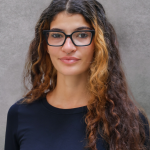 Girl with curly dark brown and blonde hair with black glasses and a black shirt